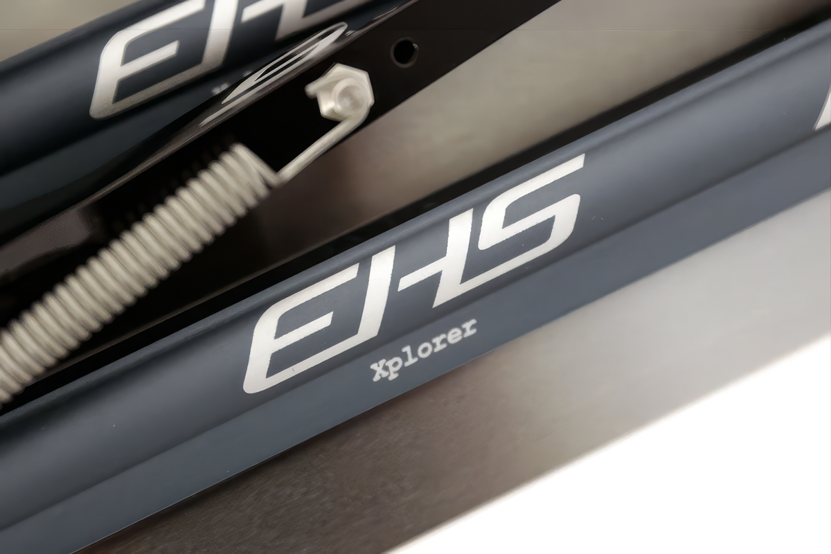 ใบมีดแคลปสปีดสเก็ตลองแทร็ก EHS StayBent Xplorer ภาพมาโครตัวอักษร EHS Xplorer บนท่อสีฟ้าเทา